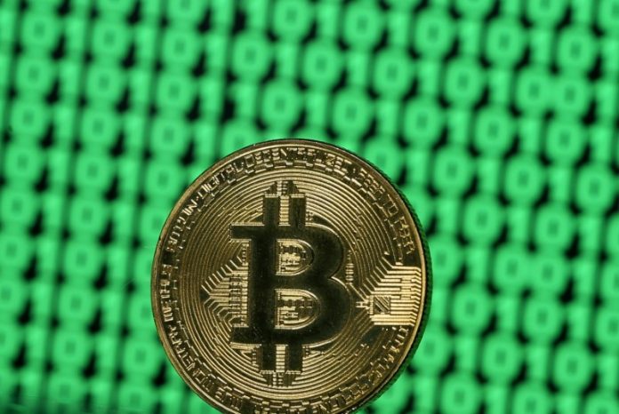 FILE PHOTO: Bitcoin token is seen placed on a monitor that displays binary digits in this illustration picture Използването на биткойни за кредитиране дава възможност да се избегне SWIFT
