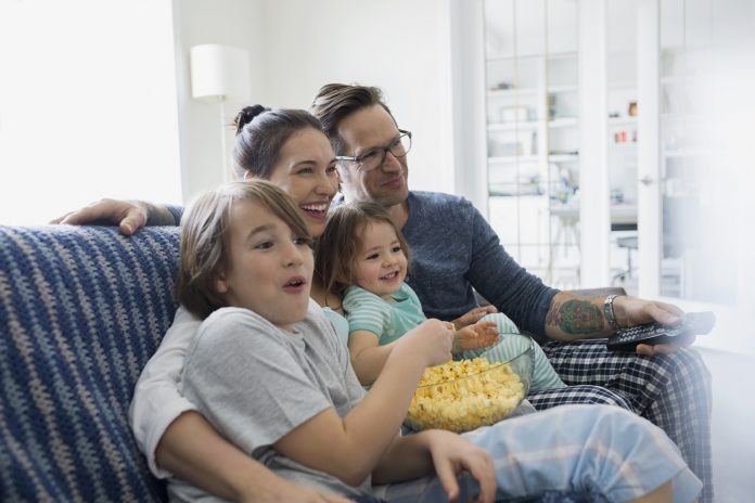 Family in pajamas watching TV and eating popcorn Нова сателитна ТВ платформа за държавите от бивша Югославия от Телеком Сърбия и SES